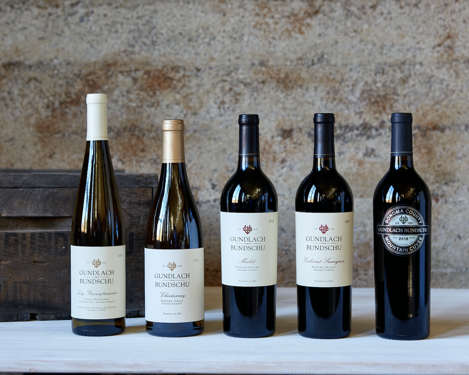 5 wine bottles on a table with a cement background and apple box behind them