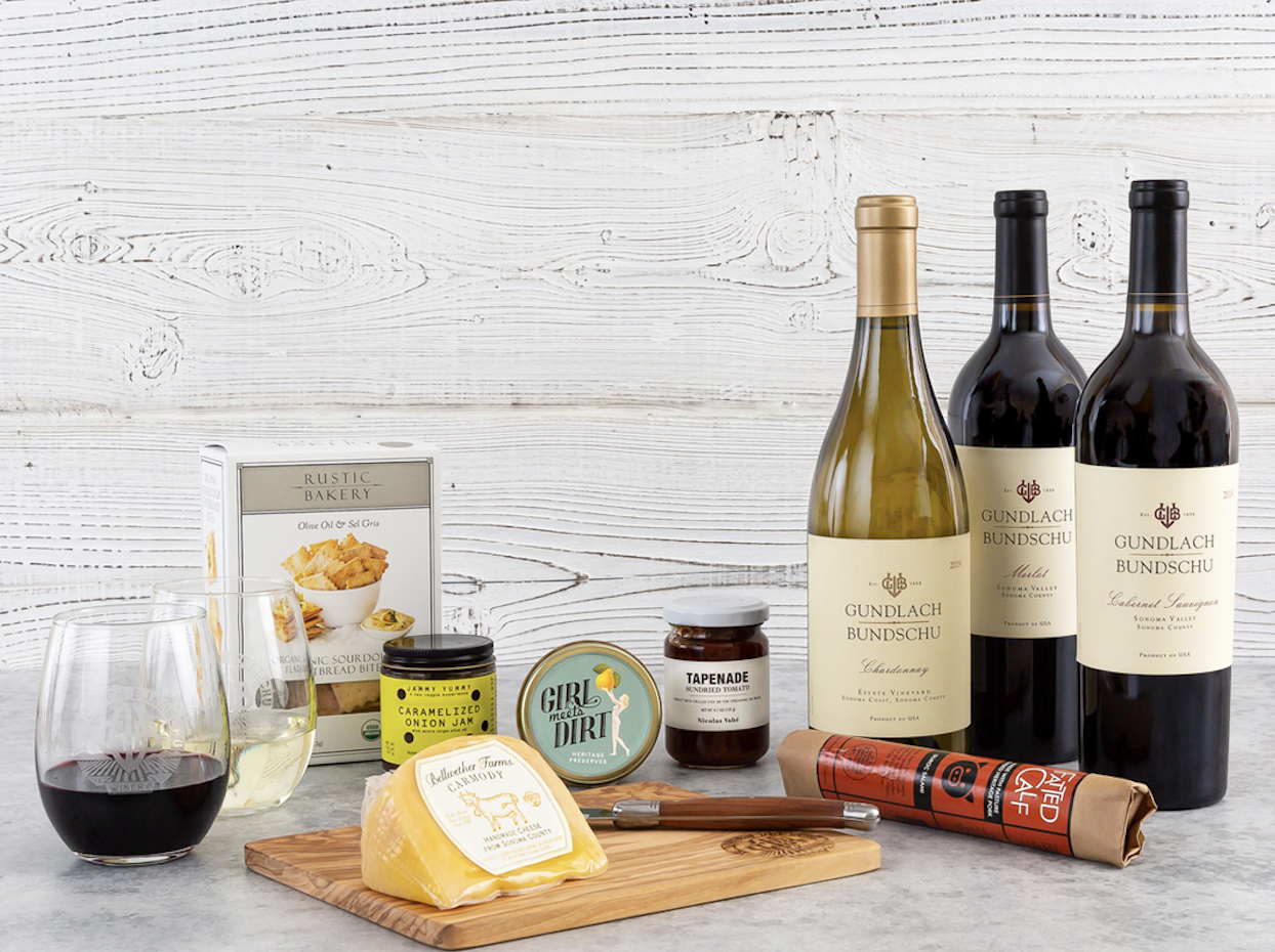 Two glasses of wine, six appetizers and three bottles of wine on a marble table with a white wooden background