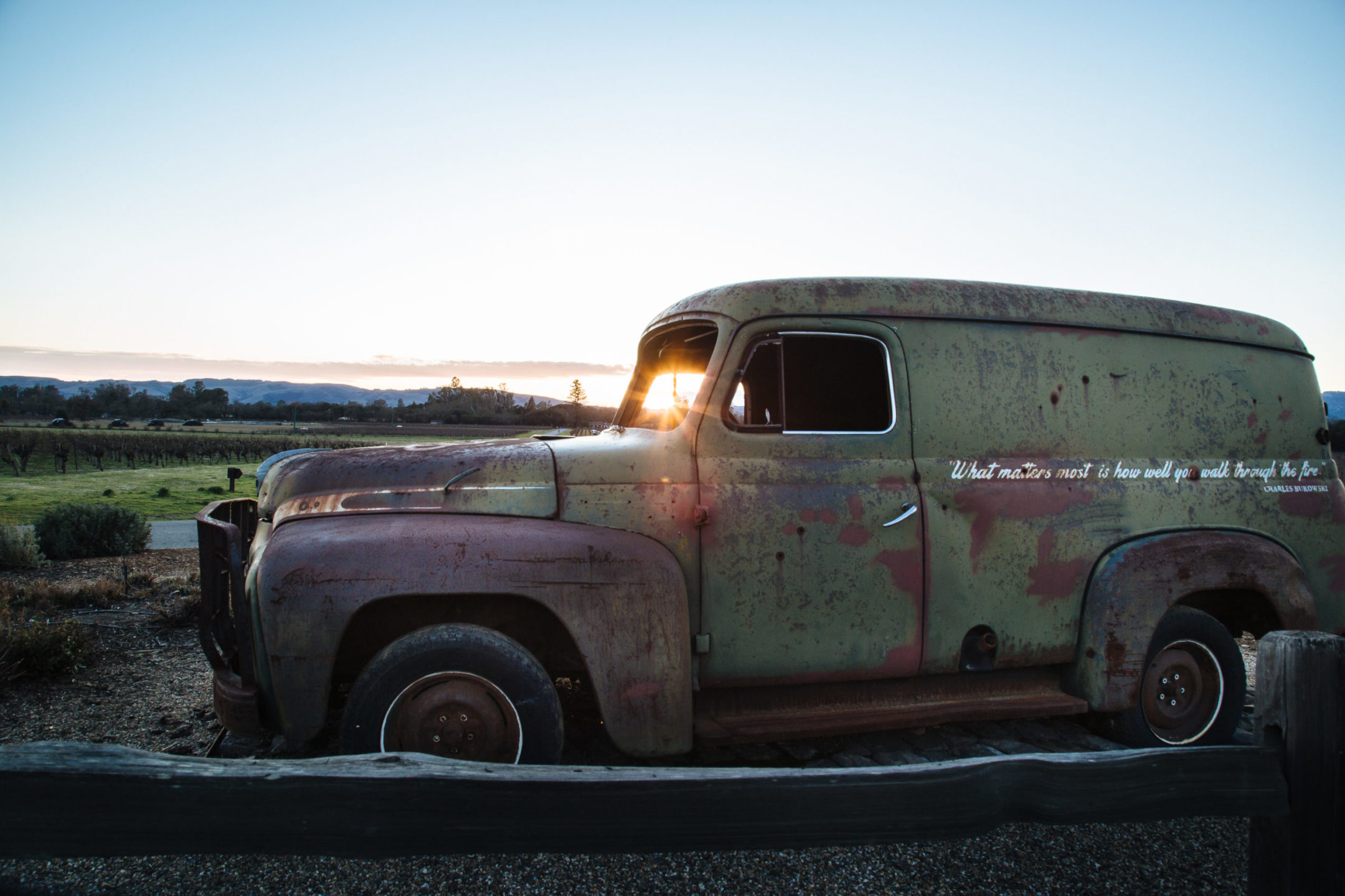 Old green sedan at sunset behind a wooden fence