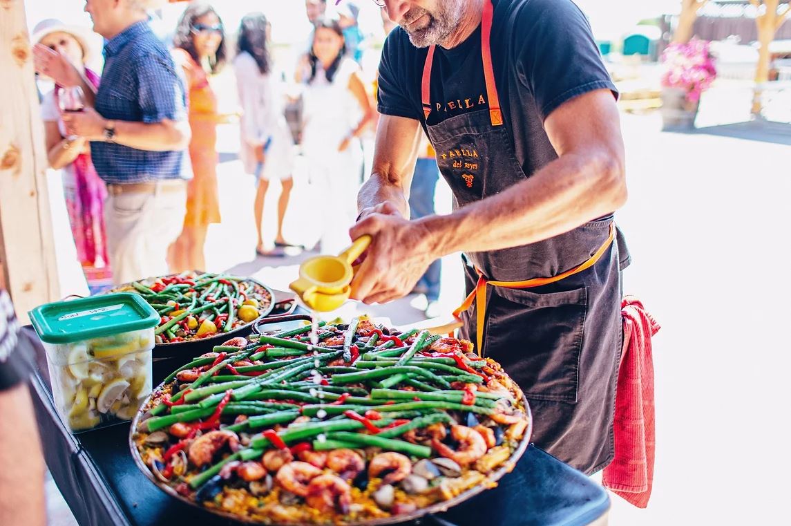 man squeezing a lemon juicer over a big pan of food