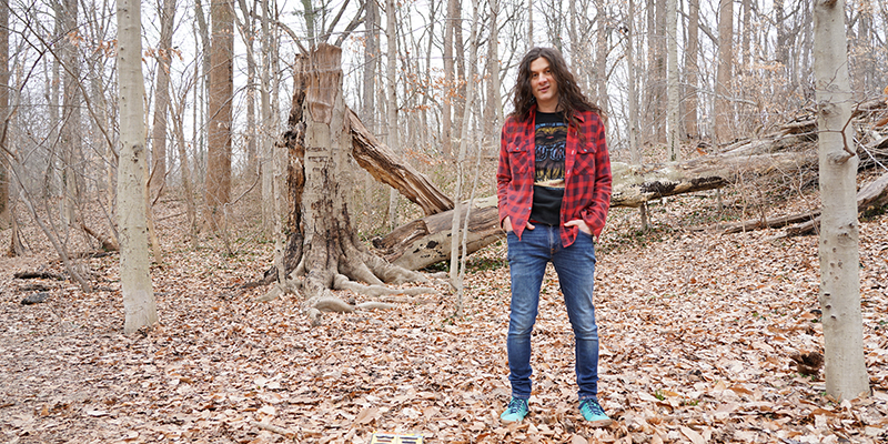 Person in blue jeans and red flannel shirt standing amongst brown trees with no green leaves