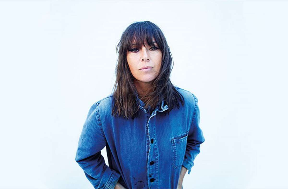 Woman with dark hair in jean shirt leaning forward against a white background
