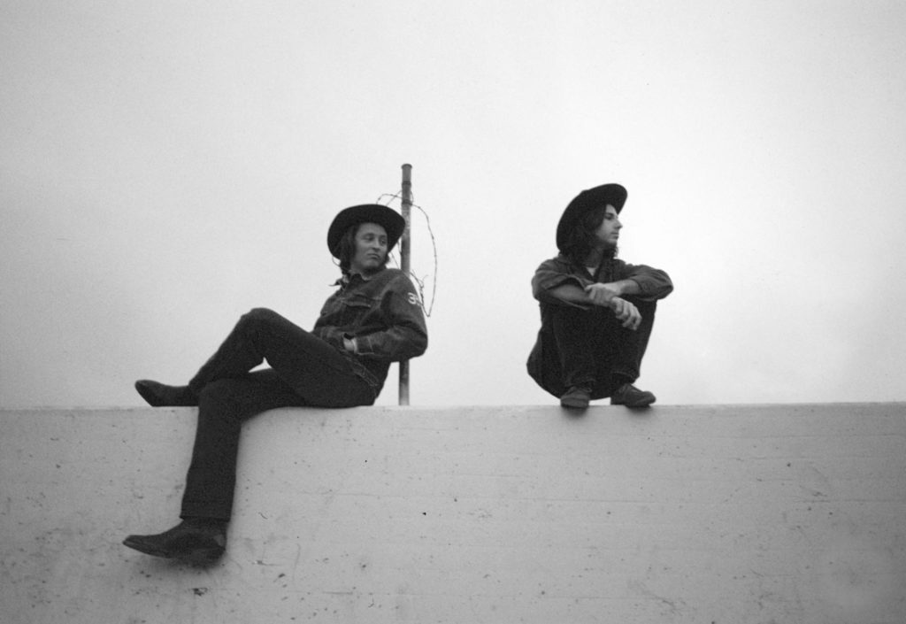 two men in hats sitting on wall on man is leaning against a pole