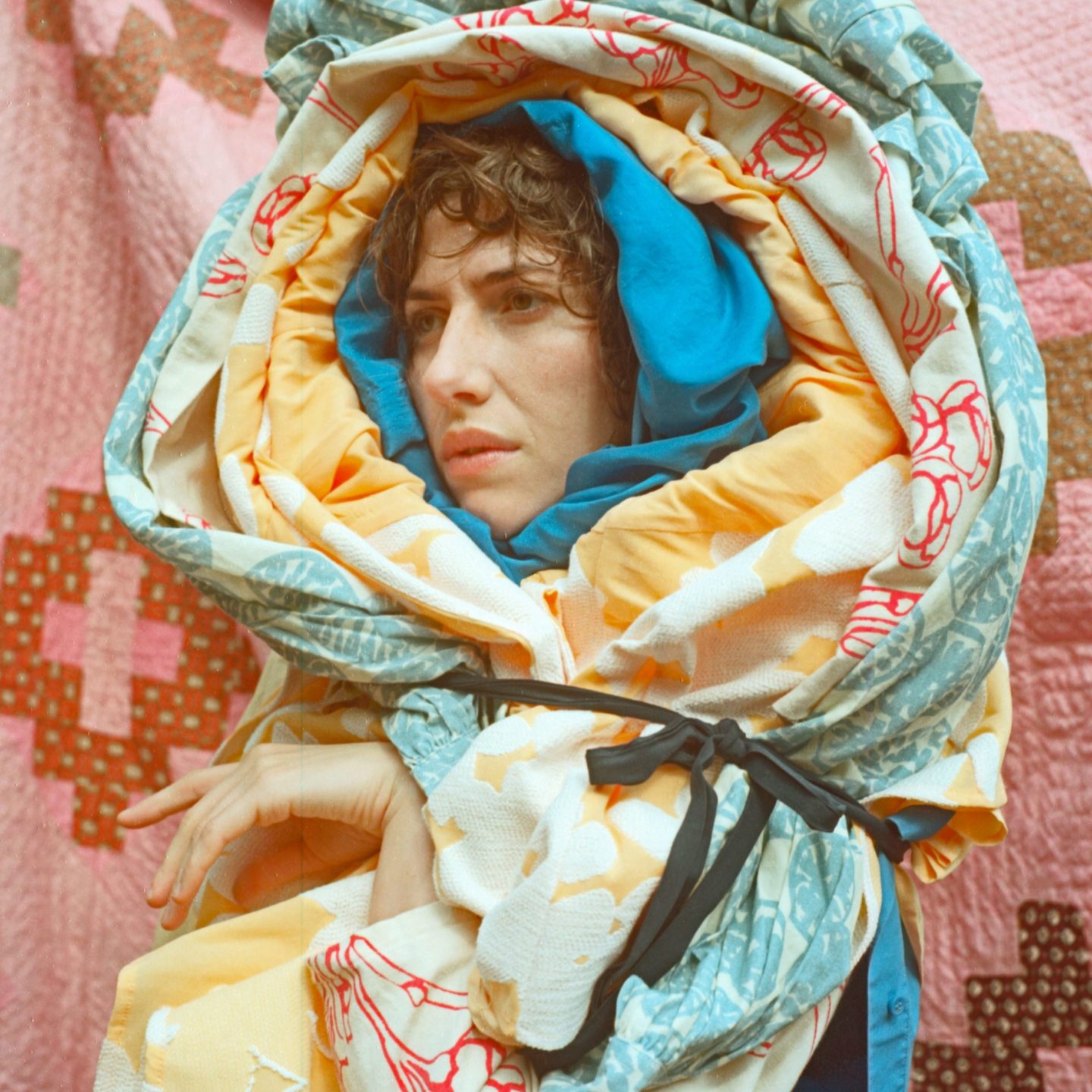 Person with brown hair wrapped in colored quilt blanket
