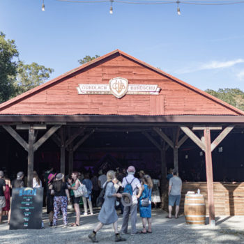 People milling about in front of a red barn with a Gundlach Bundschu logo on the top