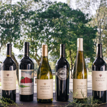 Six bottles of Gundlach Bundschu wine on a grey ledge with trees in the background