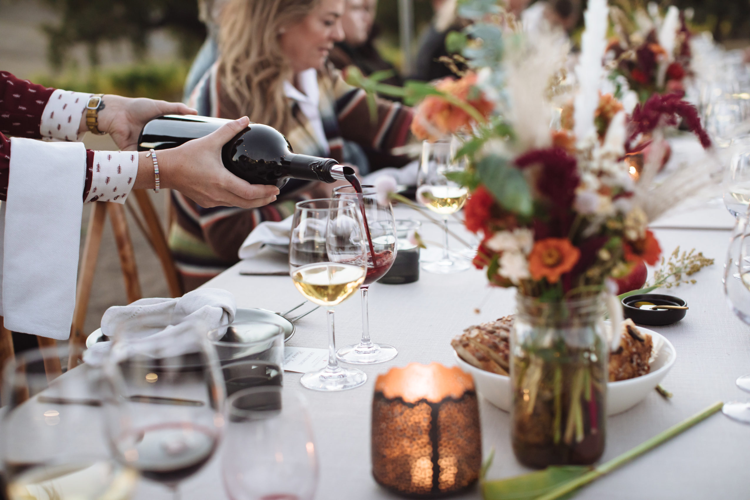 Two hands pouring a bottle of red wine in a dinner table